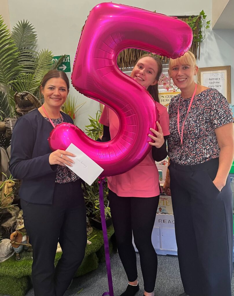 Katie celebrates five years at Maggie's Day Nursery with two colleagues and a pink number five balloon