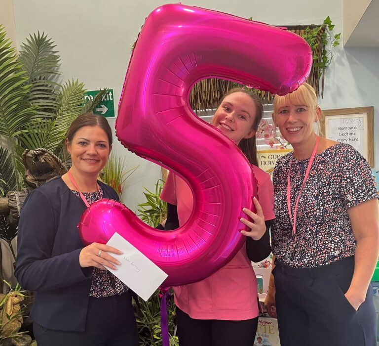 Katie celebrates five years at Maggie's Day Nursery with two colleagues and a pink number five balloon
